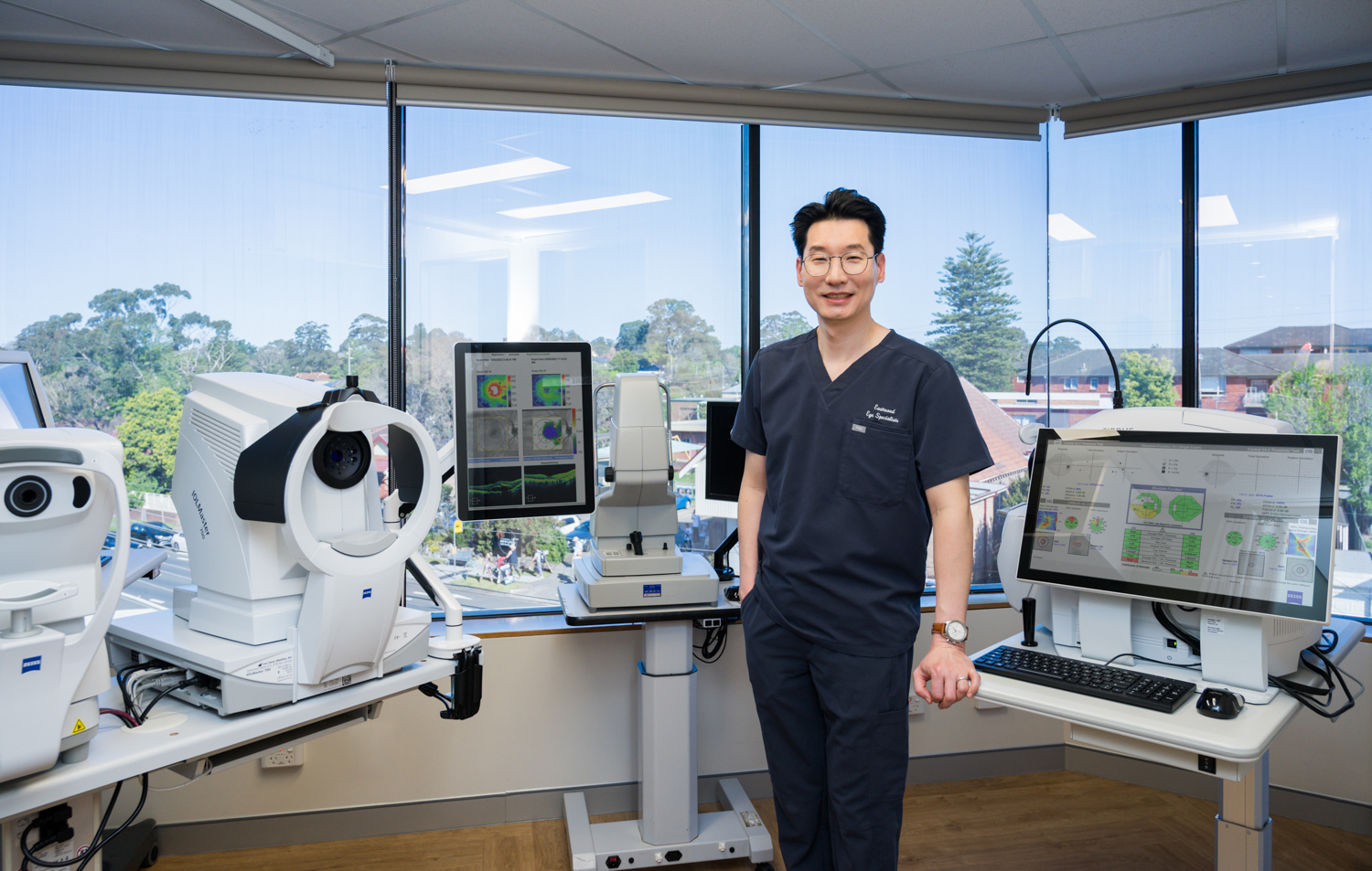 Dr Chang standing with the specialised imaging equipment used to assess patient eyes at Eastwood Eye Specialists